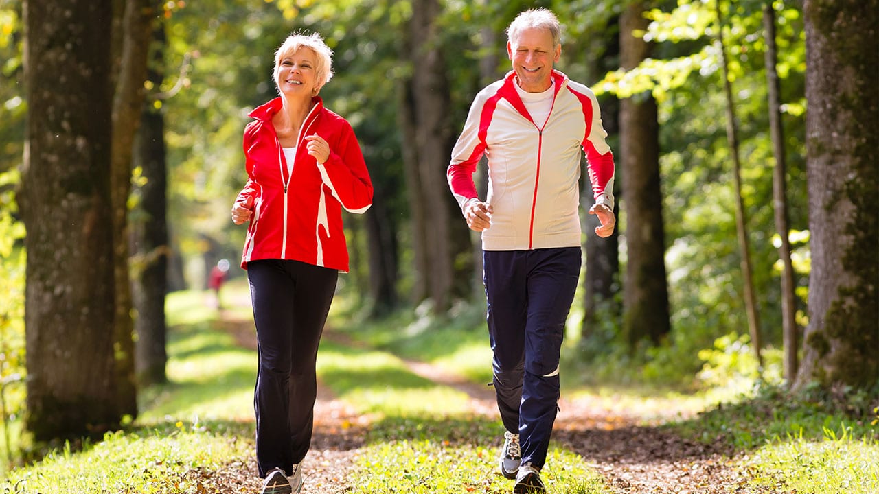 Elderly couple running together on path in the woods