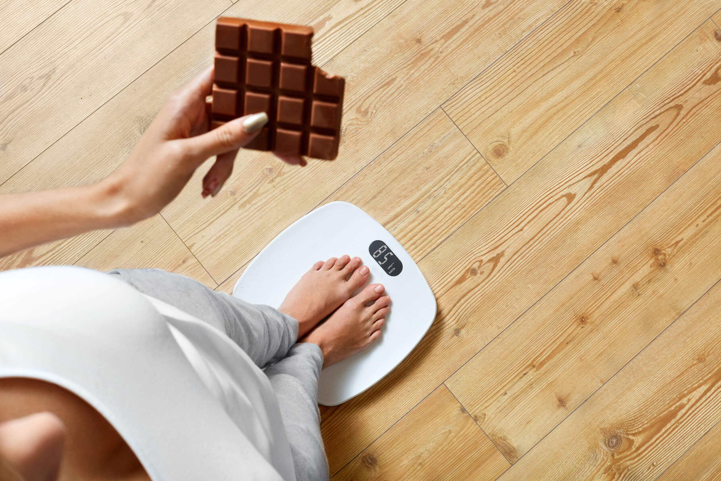 Diet. Young Woman Standing On Weighing Scale And Holding Chocolate Bar. Sweets Are Unhealthy Junk Food. Sugar Is Bad For Health. Dieting, Healthy Eating, Lifestyle. Weight Loss. Top View
