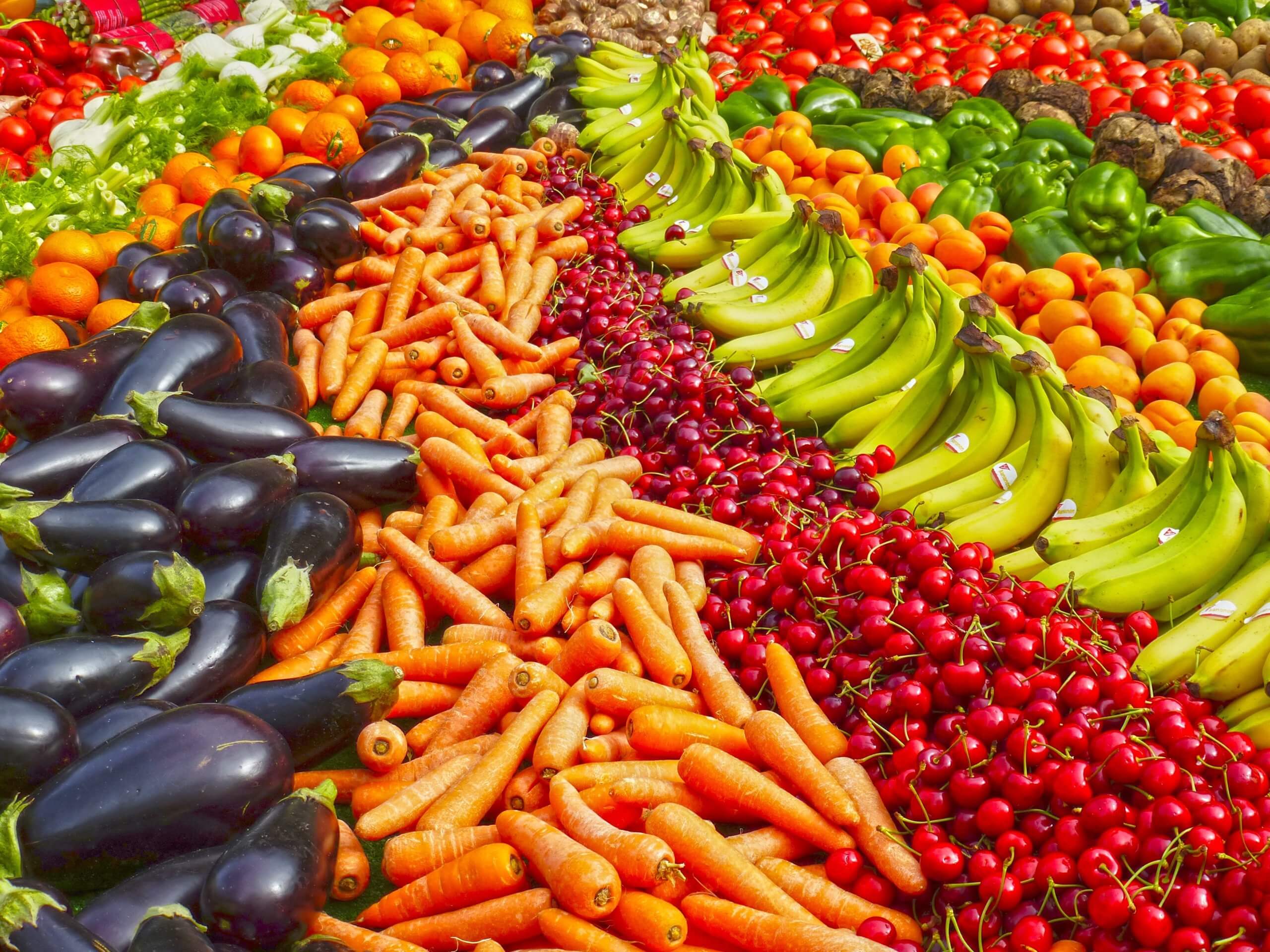 bright colored, fresh produce- eggplant, carrots, cherries, bananas, oranges, green bell peppers