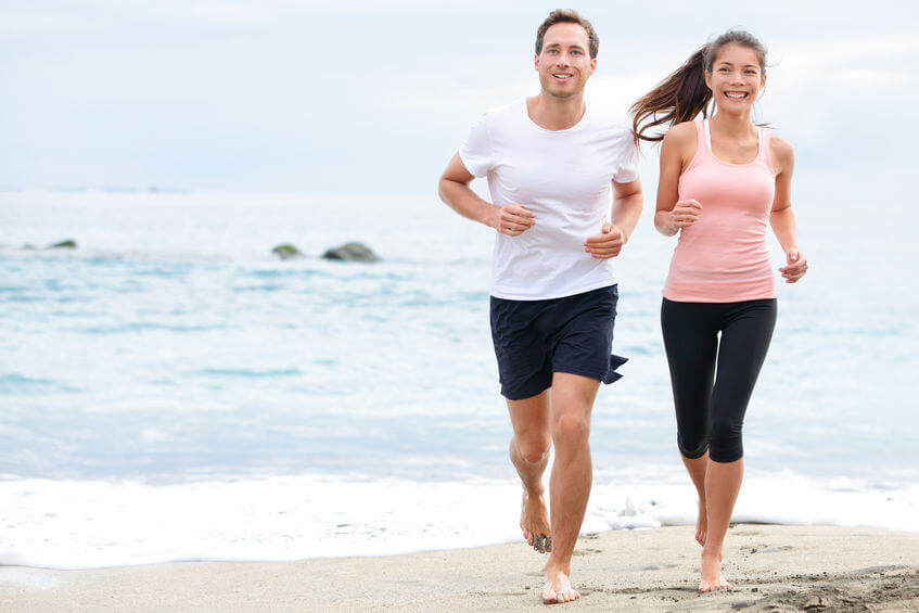 exercising running couple jogging on beach. runners training on sand by the ocean smiling happy in full body length. interracial fit fitness couple, asian woman and caucasian man runner.