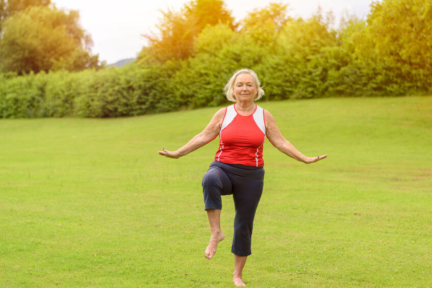 calm barefoot athletic senior woman performing yoga balancing exercises on one leg at outdoor park with green grass and copy space